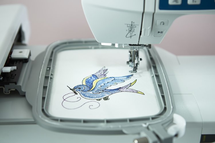 Embroidery machine stitching a colorful bird design on fabric, with the embroidery hoop holding the fabric in place.